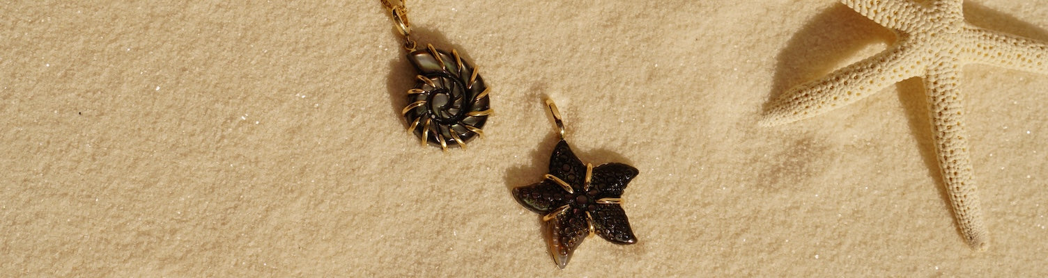 14k gold Ursula and Startfish pendant on sand beside a starfish