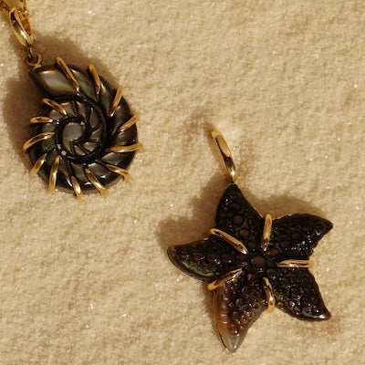 14k gold Ursula and Startfish pendant on sand beside a starfish