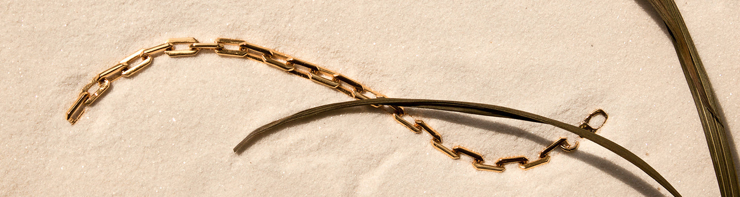 gold Sol Link Bracelet on sand with palm frond