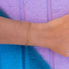 Close up of gold anchor bracelet on wrist against purple and blue background