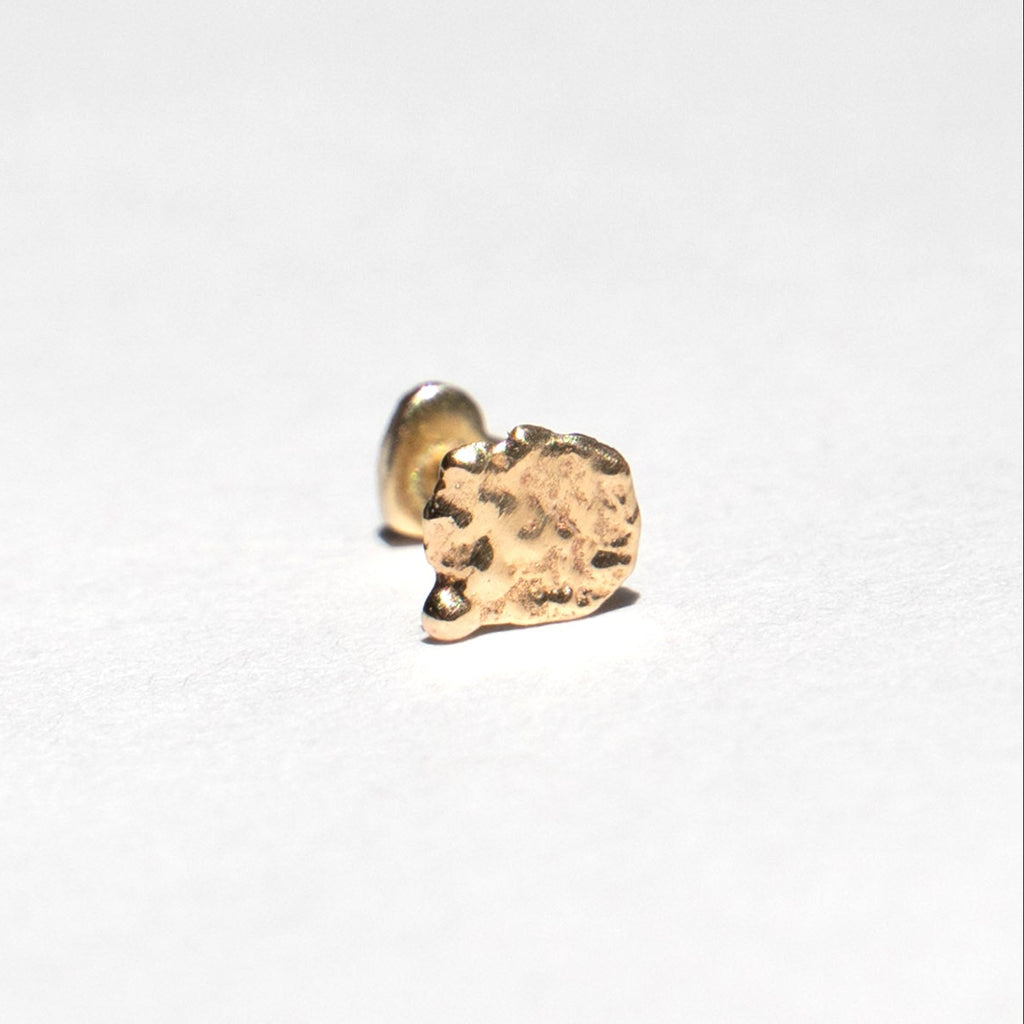 A small gold stud earring with a textured, organic shape, shown on a plain white background.