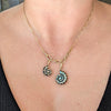 A gold chain necklace with a split pendant design, featuring one small spiral shell charm and one larger nautilus-style spiral charm with gold claw setting, worn on a model's neck.