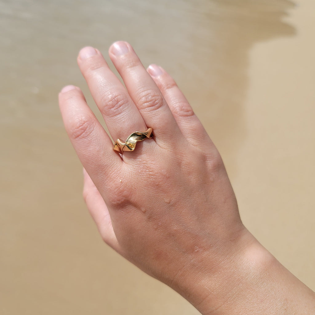 Hand wearing a gold ring on a sandy background