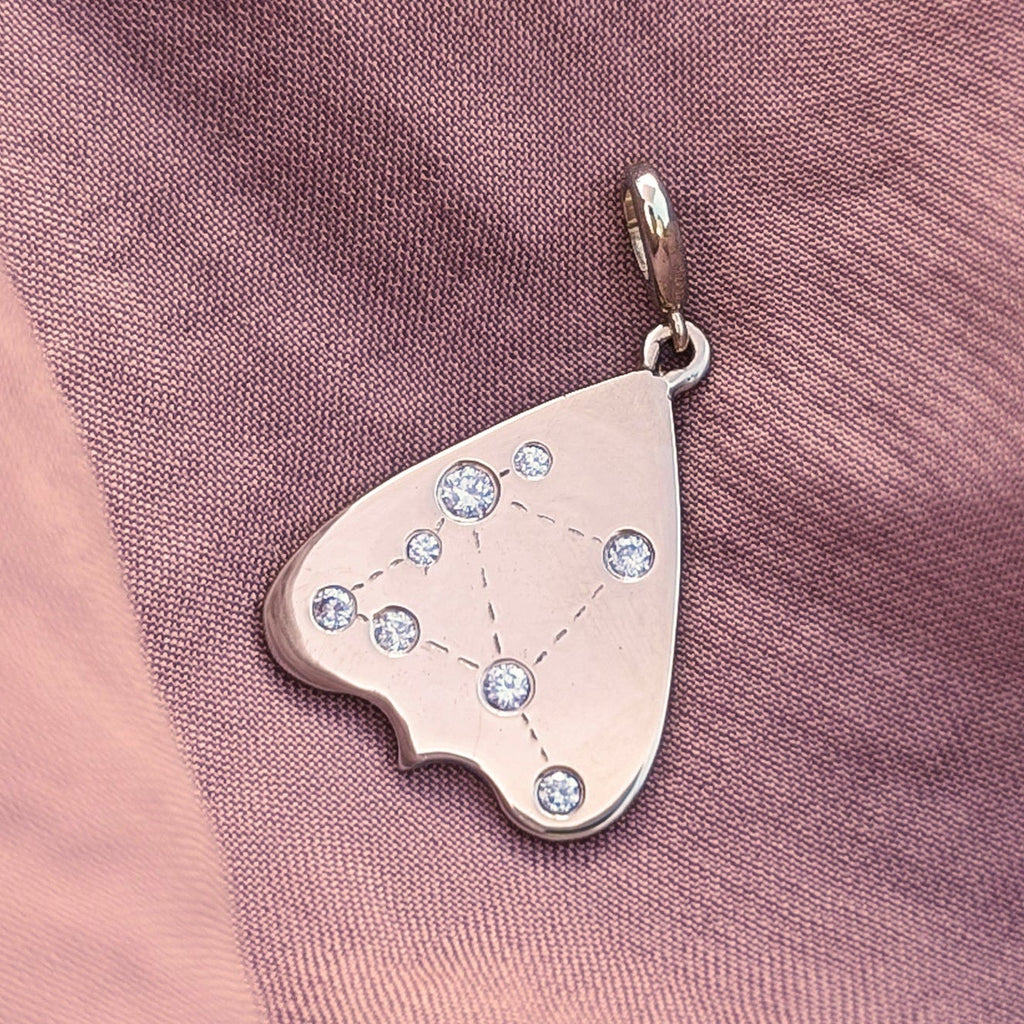 Gold and diamond constellation planchette charm pendant on a pink fabric background