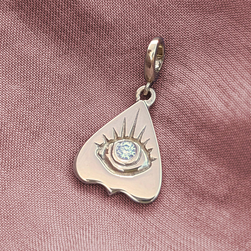 Gold pendant with a heart shaped planchette design and diamond gemstone on a pink fabric background