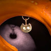 A small gold pendant shaped like a cat head with two white circular eyes, suspended from a chain, photographed against a dark background with a bright orange curved object framing the shot.