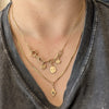 A close-up of a person wearing layered gold necklaces, including a chain necklace with star and cat-shaped charms, a delicate chain necklace with a skull charm, and a longer chain with a small diamond-shaped pendant, styled with a dark gray graphic t-shirt.