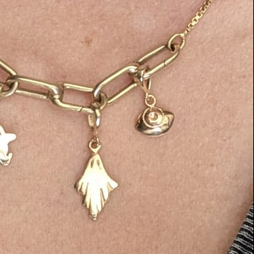 A close-up of a person wearing a  gold chain necklace with star, paperclip, and small ghost and eye charm pendants,