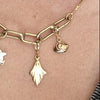 A close-up of a person wearing a  gold chain necklace with star, paperclip, and small ghost and eye charm pendants,