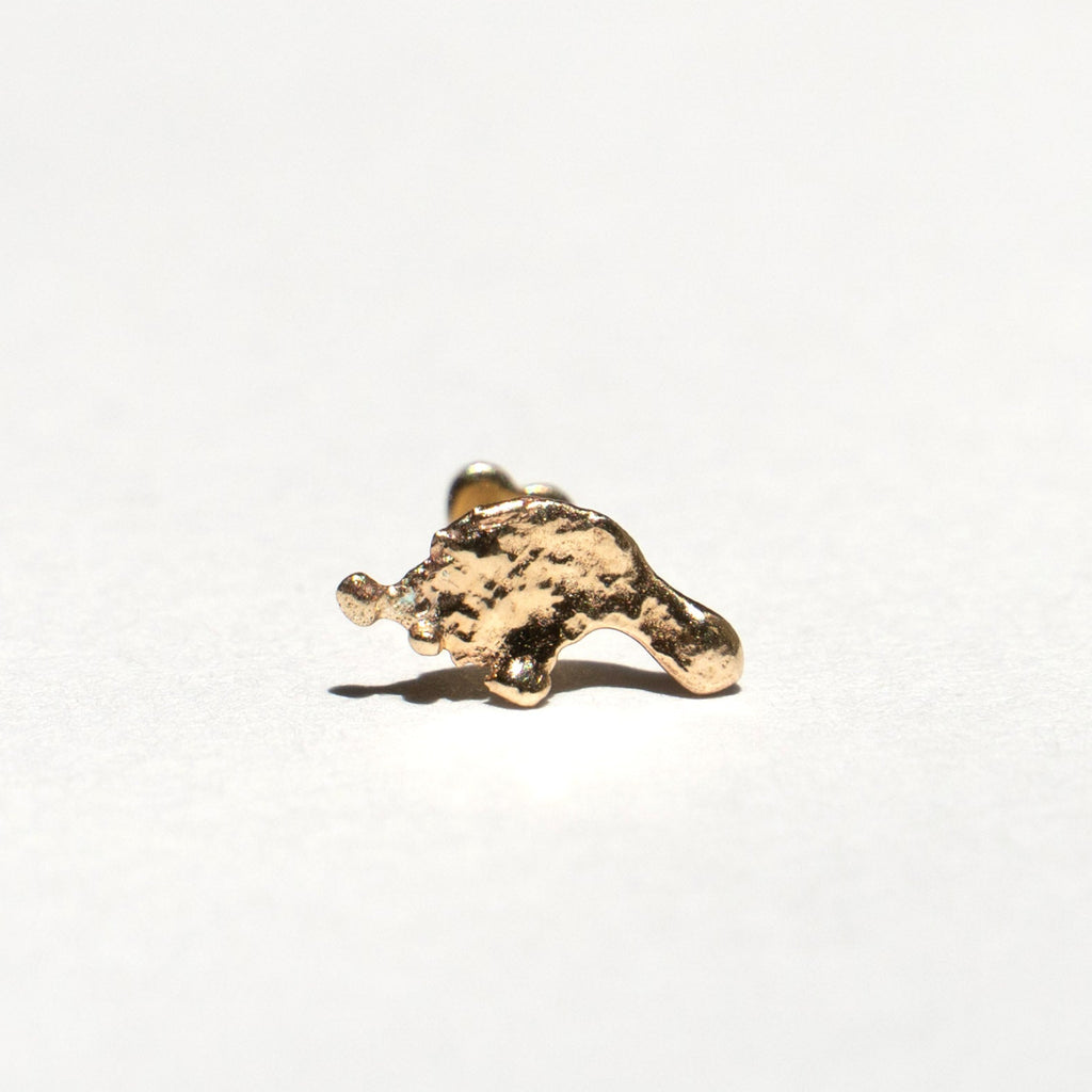A small, rough, textured gold piece, resembling a miniature gold nugget or abstract gold chunk, displayed on a clean white surface with a soft shadow.