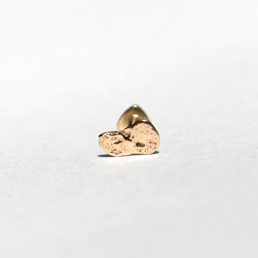 A small textured gold stud earring with a polished backing, shown on a plain white surface.