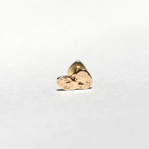 A small textured gold stud earring with a polished backing, shown on a plain white surface.