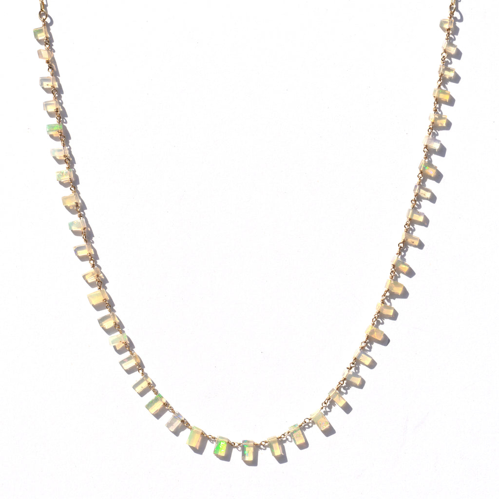 A delicate gold chain necklace featuring small, irregular, faceted opal stones that shimmer with cream, beige, and vibrant green iridescence, displayed against a clean white background.