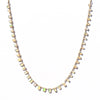 A delicate gold chain necklace featuring small, irregular, faceted opal stones that shimmer with cream, beige, and vibrant green iridescence, displayed against a clean white background.