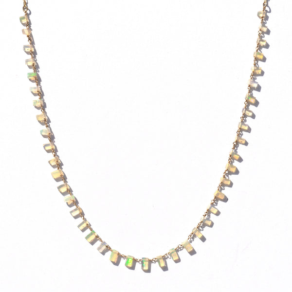 A delicate gold chain necklace featuring small, irregular, faceted opal stones that shimmer with cream, beige, and vibrant green iridescence, displayed against a clean white background.