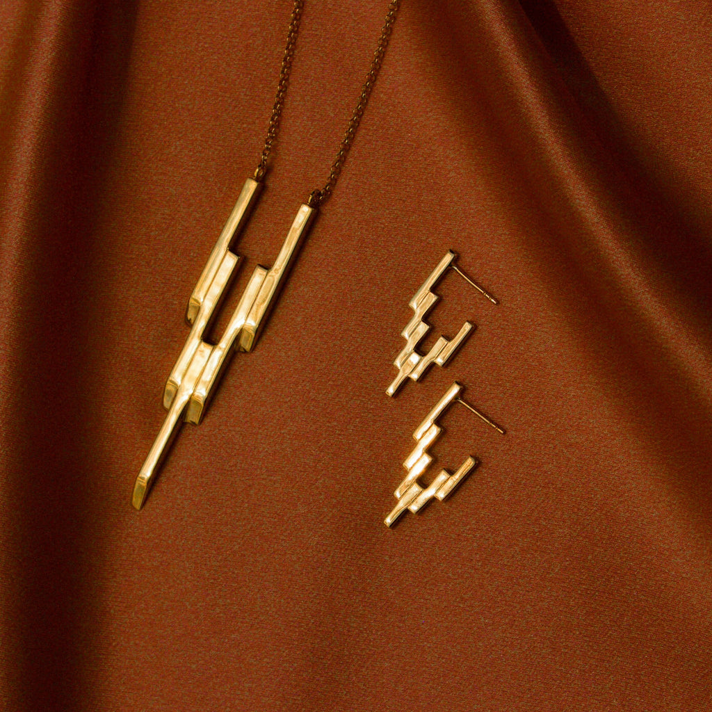 After Glow Pendant and After Glow Huggies laying flat against a burnt orange satin fabric