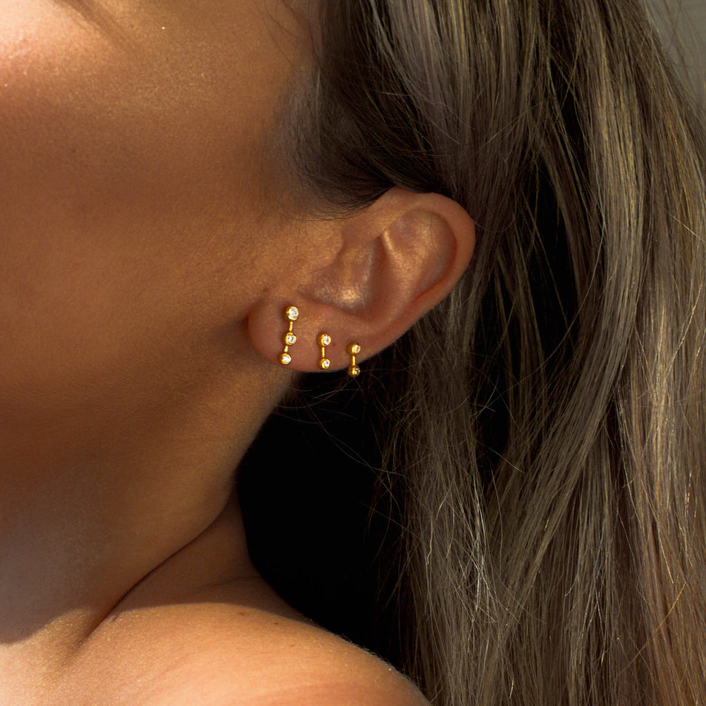 Woman wearing the Large and Small Gold Star Dust Studs with White Topaz, layered on her ear