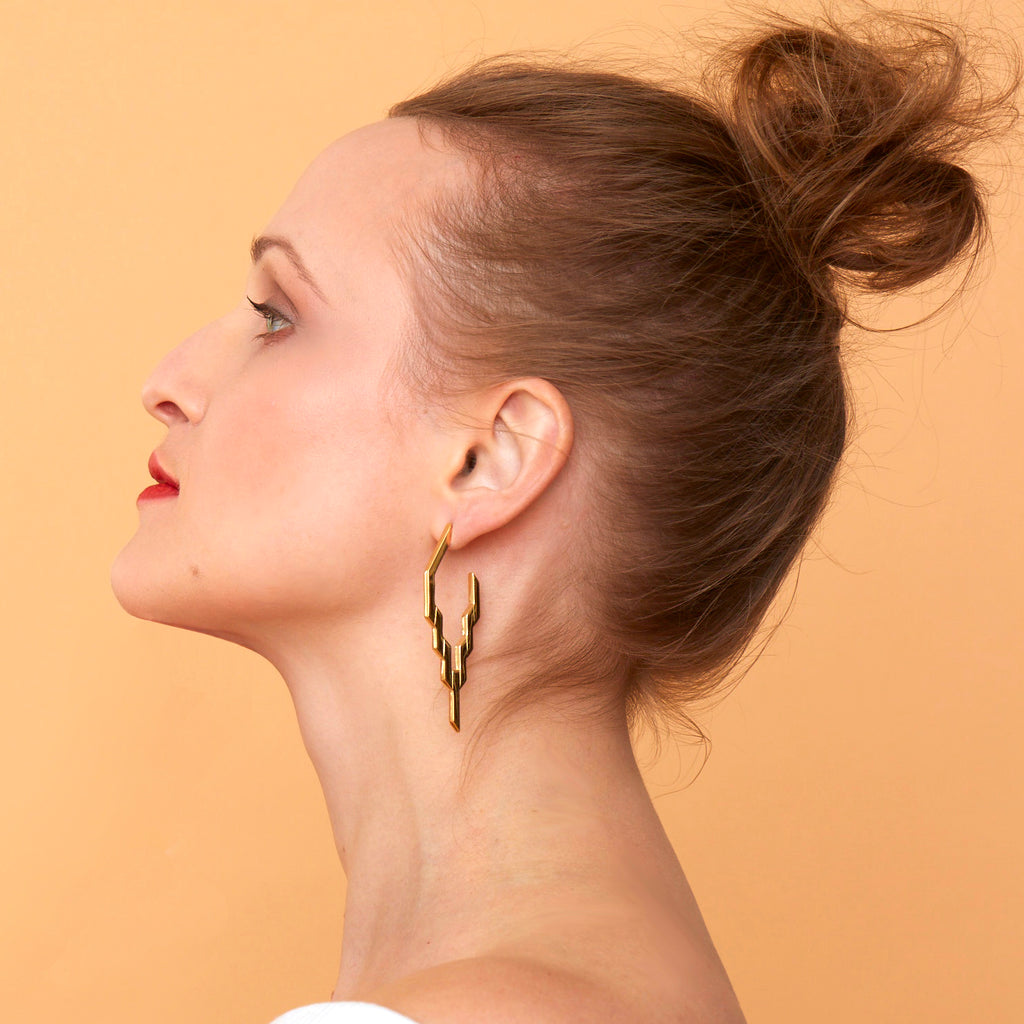 Profile of woman against a Apricot toned background, wearing the Gold After Glow Hoops